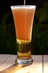 one glass of light beer.  lager with beer foam on a wooden table on dark blured background