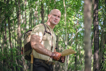 Adventurer man is learning an old map in the green forest thickets.
