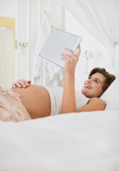 Obraz na płótnie Canvas Pregnant woman using tablet computer on bed