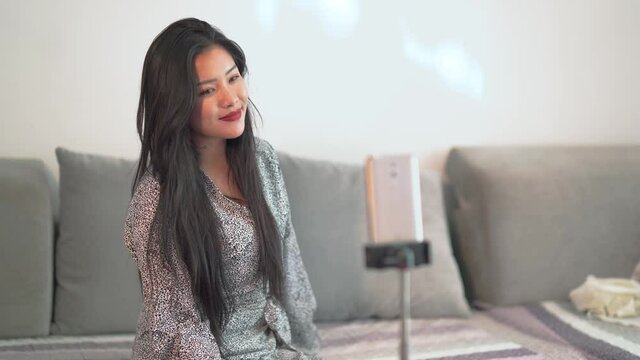 Chinese girl influencer takes selfie at home. Narcissistic pretty China woman takes self photos to post on social media. Female posing for cell phone shots.