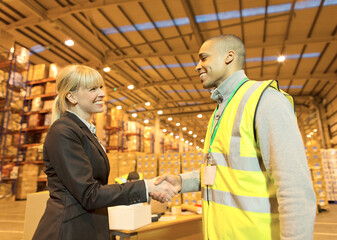 Businesswoman and worker shaking hands in warehouse