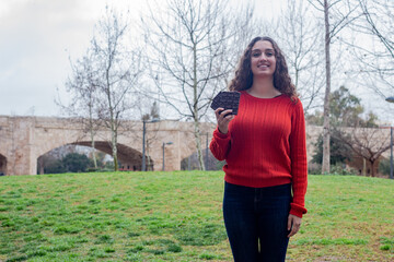 Portrait of happy attractive caucasian young woman holding chocolate, in the park, orange sweater and jeans, long curly hair. Place for your text in copy space.