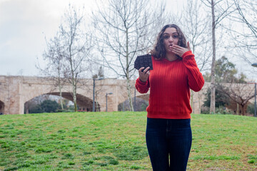 Portrait of happy attractive caucasian young woman model with chocolate. Covered mouth with hand smiling, in the park, long curly hair. Place for your text in copy space.