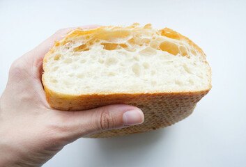 Half of fresh white bread, ciabatta with a crust, in the hand of a young woman, on a white background. The texture of the bread in the cut. Baking, cooking, breakfast. A piece of bread 