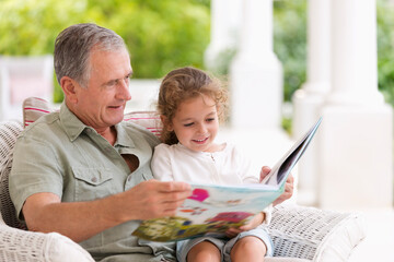 Older man reading to granddaughter on porch