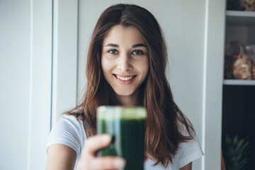 Cheerful caucasian woman with black hair posing with a fresh green juice and smile at camera