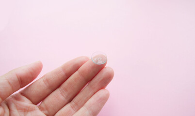 soft lens for the eyes on the fingers of the hands of a young girl, on a pink background. Wearing...