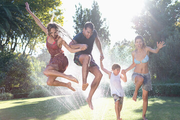Family jumping in sprinkler - obrazy, fototapety, plakaty