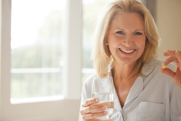 Portrait of smiling woman holding pill and glass of water