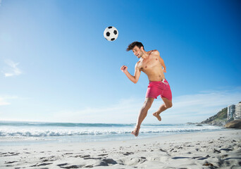 Man in swim trunks heading soccer ball on beach © Dan Dalton/KOTO