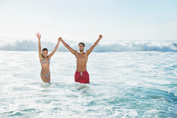 Portrait enthusiastic couple holding hands with arms raised in ocean