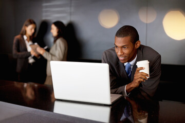 Smiling businessman drinking coffee and using laptop