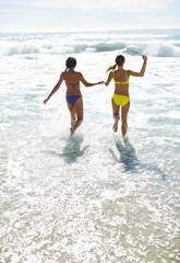 Friends in bikinis holding hands and running into ocean