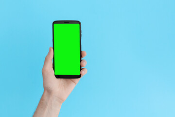 Smartphone with a green screen in left hand on an light blue background.