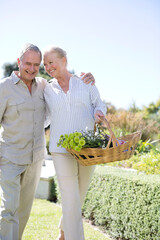 Senior couple walking in garden with basket of flowers