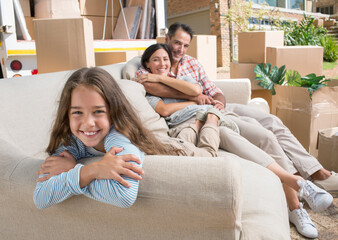 Portrait of smiling family on sofa in driveway near moving van