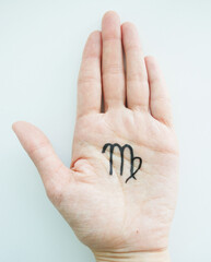 On the palm of a young girl is a top view, with a black felt-tip pen the zodiac sign Virgo is drawn, on a light background. Features, characteristics of the sign of Virgo in the palm of your hand, 