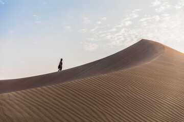 Fototapeta na wymiar woman walking to the top of a dune in the desert