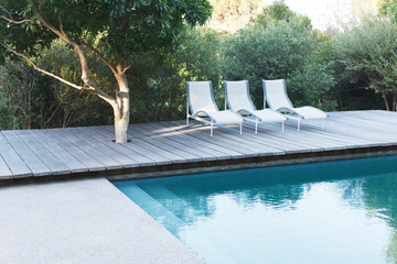Wooden deck and lounge chairs by swimming pool