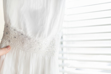 white dress for the bride with rhinestones and lace on the background of a bright window with jalousie