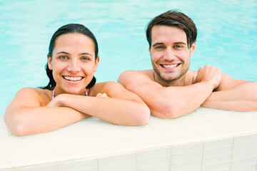 Portrait of smiling couple leaning at edge of swimming pool