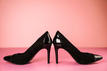 Close up of stylish black high heels shoes on a pink table with a light pink background.