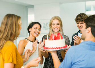 Friends clapping around woman with birthday cake