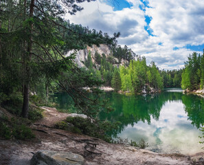 Lake with beautiful reflections of clouds in blue sky and ancient pines growing in rock city...
