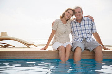 Senior couple dipping feet in swimming pool - Powered by Adobe