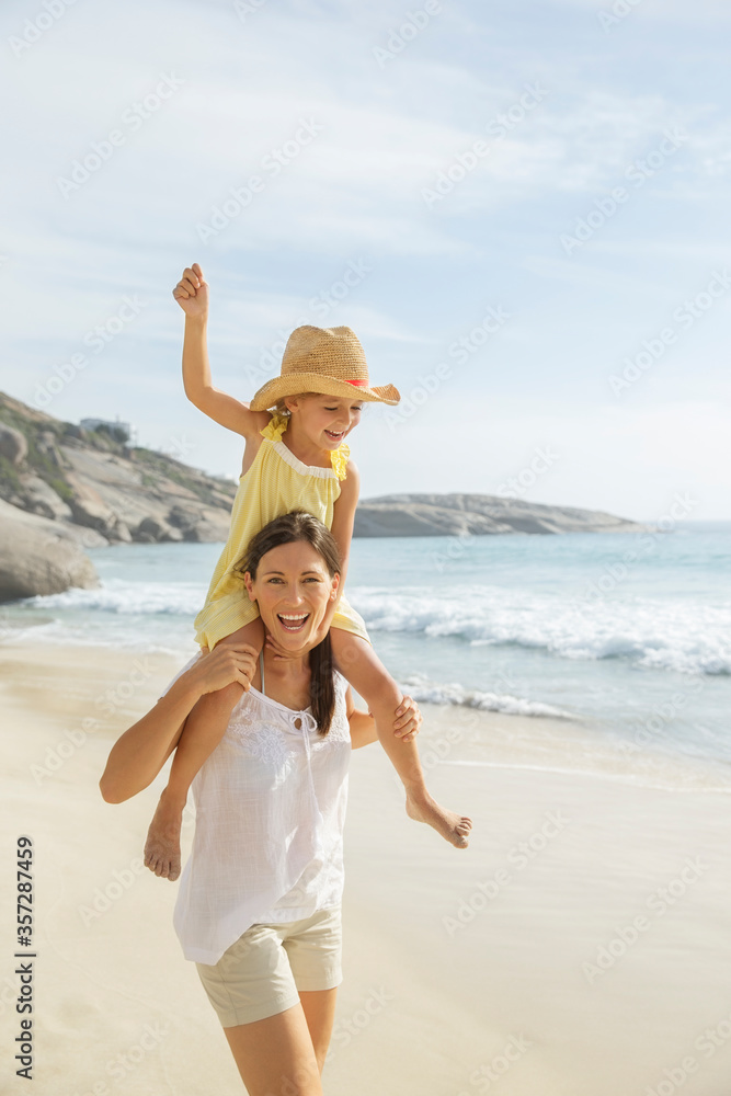 Wall mural Mother carrying daughter on shoulders on beach