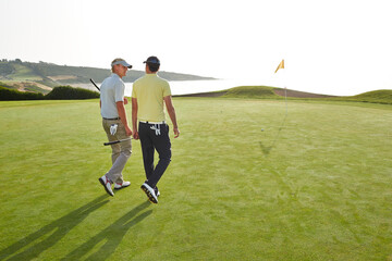 Men walking toward hole on golf course overlooking ocean