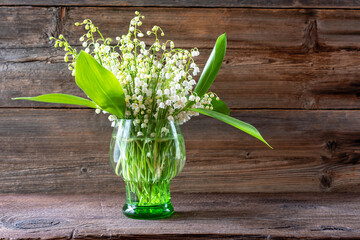 Spring flowers lilies of the valley in a vase on a wooden background.