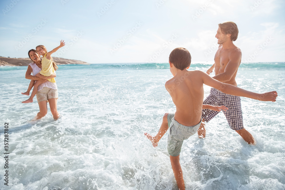 Poster family playing together in waves on beach