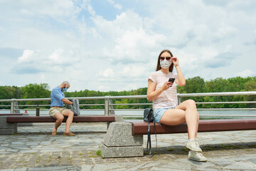A woman on a bench keeping a social distance with a man sitting on another bench with backpack on...