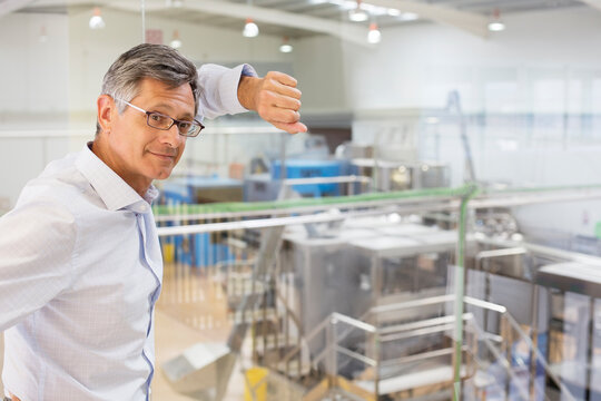 Businessman Leaning On Window Overlooking Factory