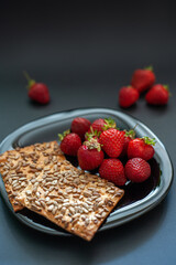 Fresh strawberries on a black plate on a black background. Dry cookies with seeds. A healthy snack. A light breakfast with berries. Diet snack with strawberries.