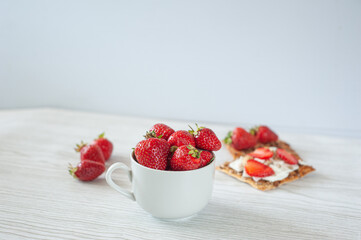 Strawberries in a cup on a light wooden background. Biscuits with cheese, strawberries and hazelnuts. Dietary nutrition. Summer breakfast. A healthy snack.