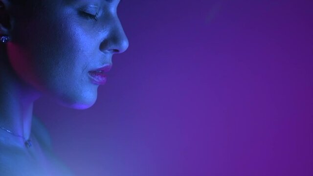 Colorful portrait of beauty model girl. Beautiful woman face closeup. UV lights. Gorgeous Brunette girl in neon light. Beauty Glamour sensual lady posing. Disco. 4K Slow motion