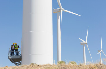 Workers talking on wind turbine in rural landscape