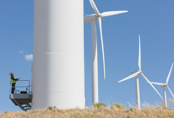 Worker examining wind turbine in rural landscape