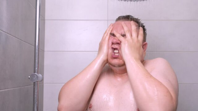 Tired man takes a rain shower, bathes under a stream of water, screams from irritation and hopelessness
