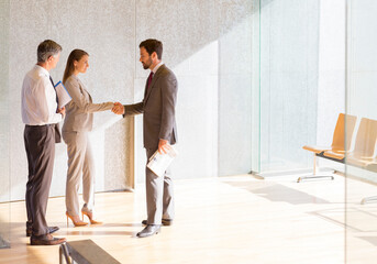 Business people shaking hands in sunny office lobby