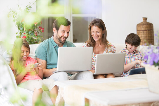 Family With Laptops, Digital Tablet And Cell Phone On Patio Sofa