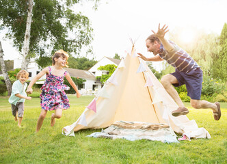Father chasing children around teepee in backyard
