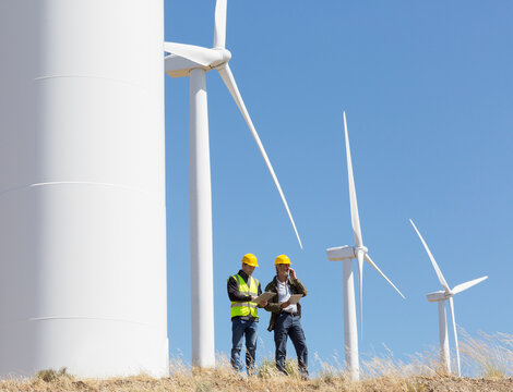 Workers talking by wind turbines in rural landscape