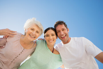 Senior woman hugging couple against blue sky