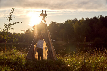 A child sits in a wigwam with a bouquet of wildflowers. Happy kids in the summer near the lake. High quality photo © Vladimir