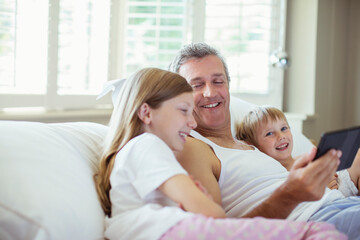 Father and children using digital tablet on bed