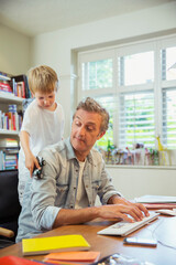 Boy distracting father at work in home office
