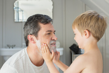 Boy rubbing shaving cream on father's face